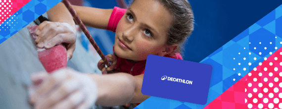 Primo piano di una bambina durante una sessione di arrampicata indoor; sulla destra è presente una gift card Decathlon. | Crédit Agricole Primo piano di una bambina durante una sessione di arrampicata indoor; sulla destra è presente una gift card Decathlon. | Crédit Agricole