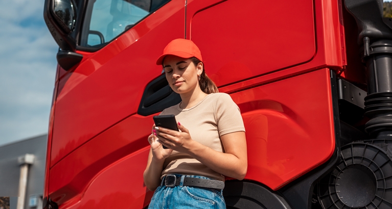 Rgazza che guarda il telefono appoggiata a un camion | Crédit Agricole Rgazza che guarda il telefono appoggiata a un camion | Crédit Agricole