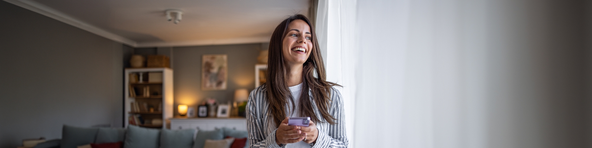 Ragazza con il telefono in mano che guarda fuori dalla finestra. | Crédit Agricole Ragazza con il telefono in mano che guarda fuori dalla finestra. | Crédit Agricole