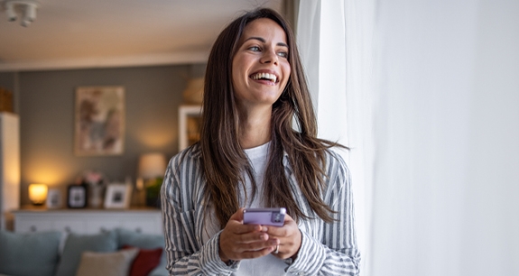 Ragazza con il telefono in mano che guarda fuori dalla finestra. | Crédit Agricole Ragazza con il telefono in mano che guarda fuori dalla finestra. | Crédit Agricole